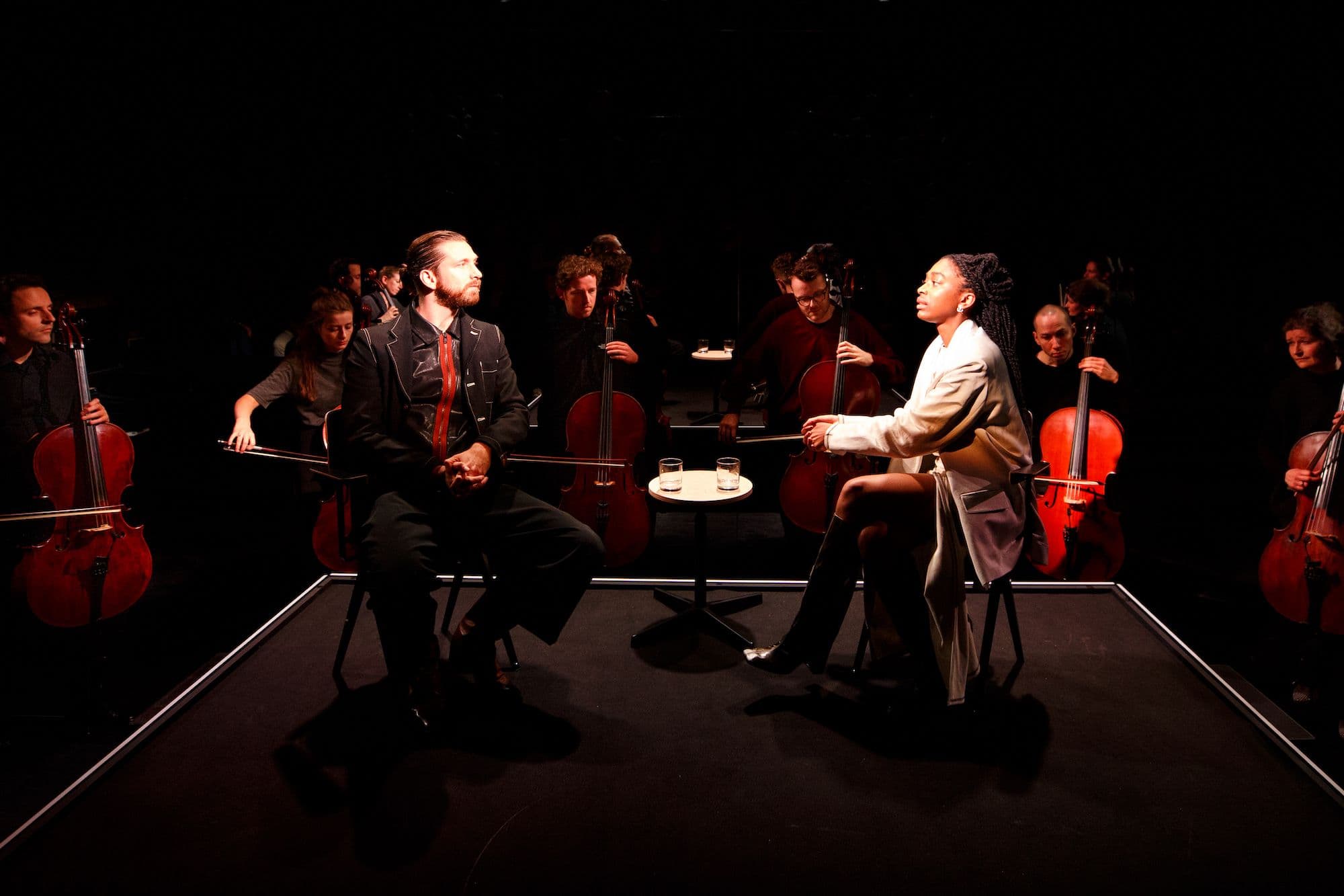 Ntianu Stuger en Vincent van der Valk zitten op het podium en zijn in gesprek, het Cello Octet achter hen